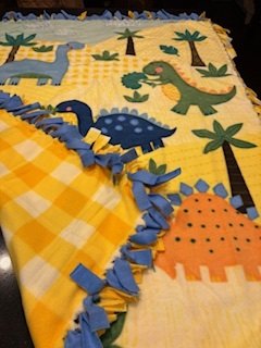 A yellow dinosaur fleece blanket with blue fringe
