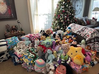 Blankets and stuffed animals collected beside a Christmas tree